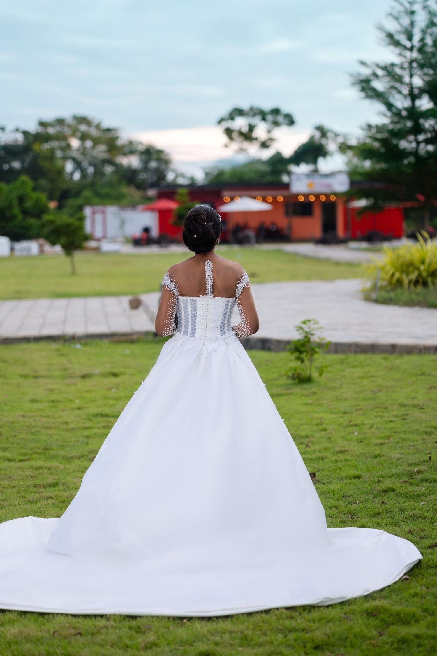 A white ballgown wedding dress with a long train spreads across a grassy lawn on a sunny day.