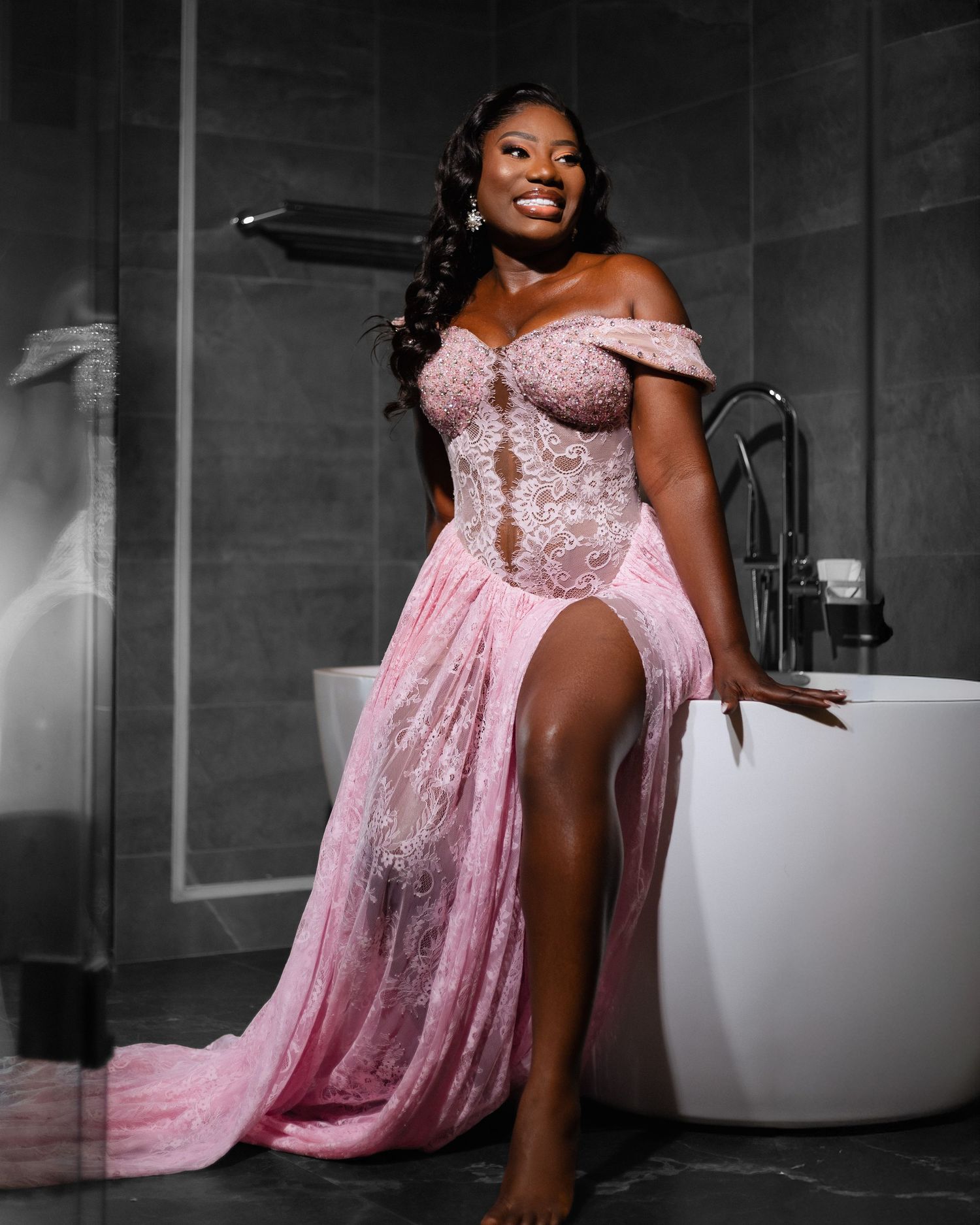 A person in an elegant pink off-shoulder gown poses gracefully in a dramatic black and white setting with selective coloring.