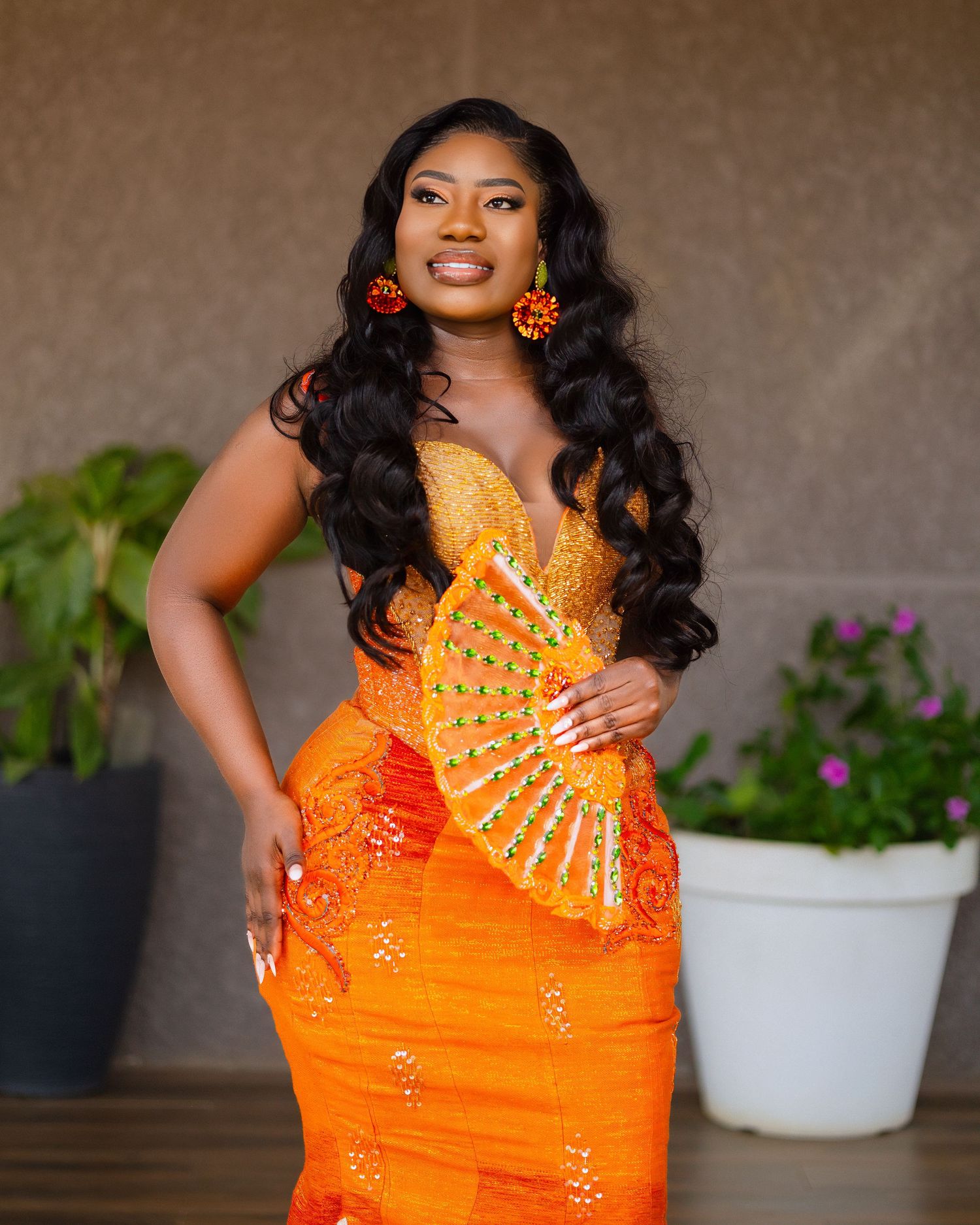 Elegant orange and yellow beaded dress with flowing long black hair and statement earrings against neutral background.