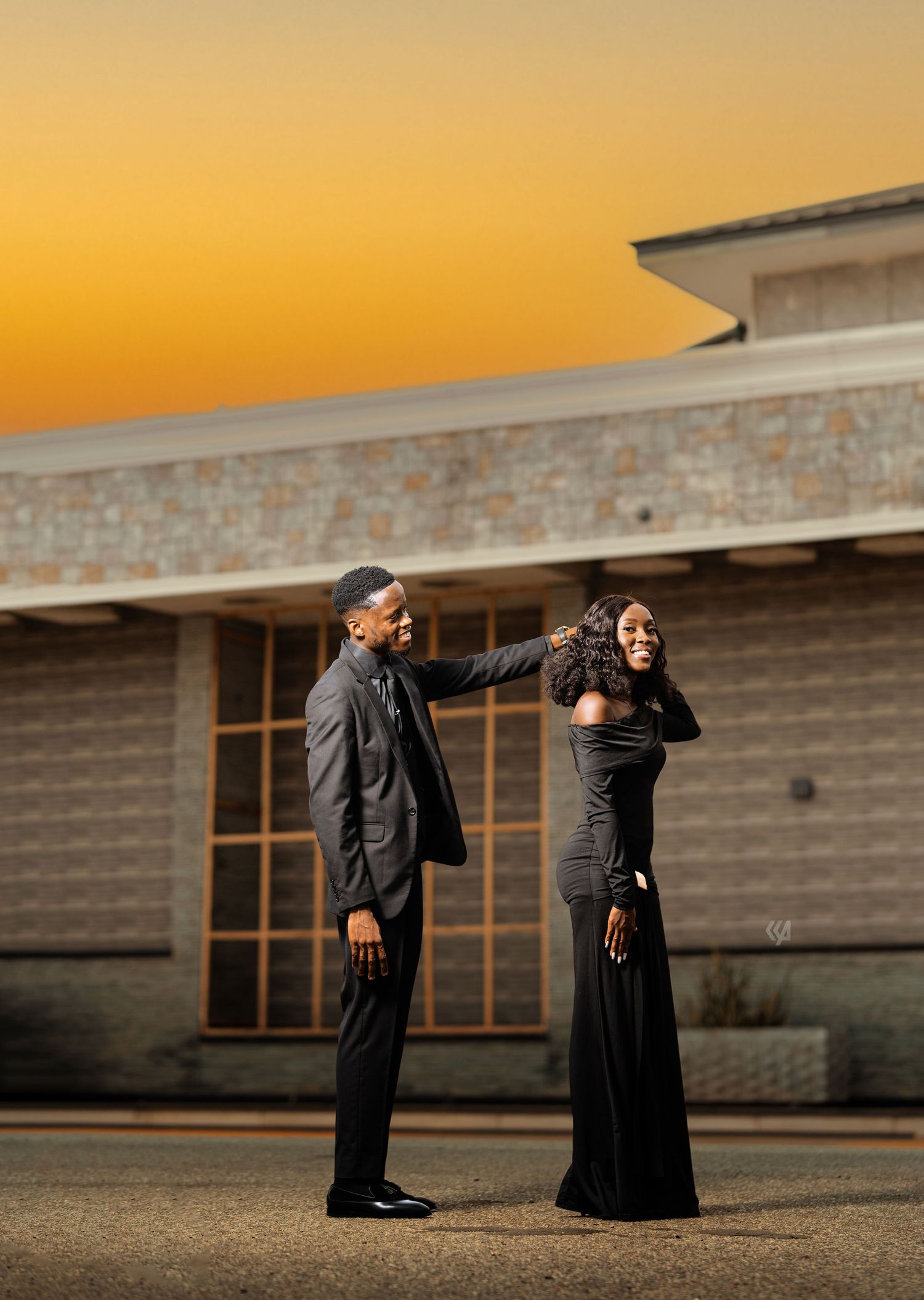 A couple poses playfully at sunset against a modern building backdrop.