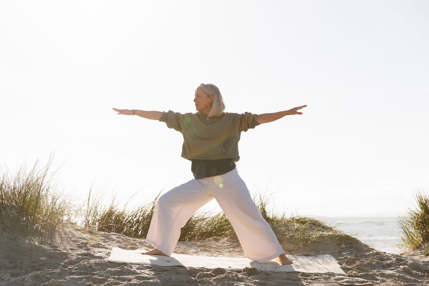 Athletic pose demonstrated on sandy beach with tall grass in background.