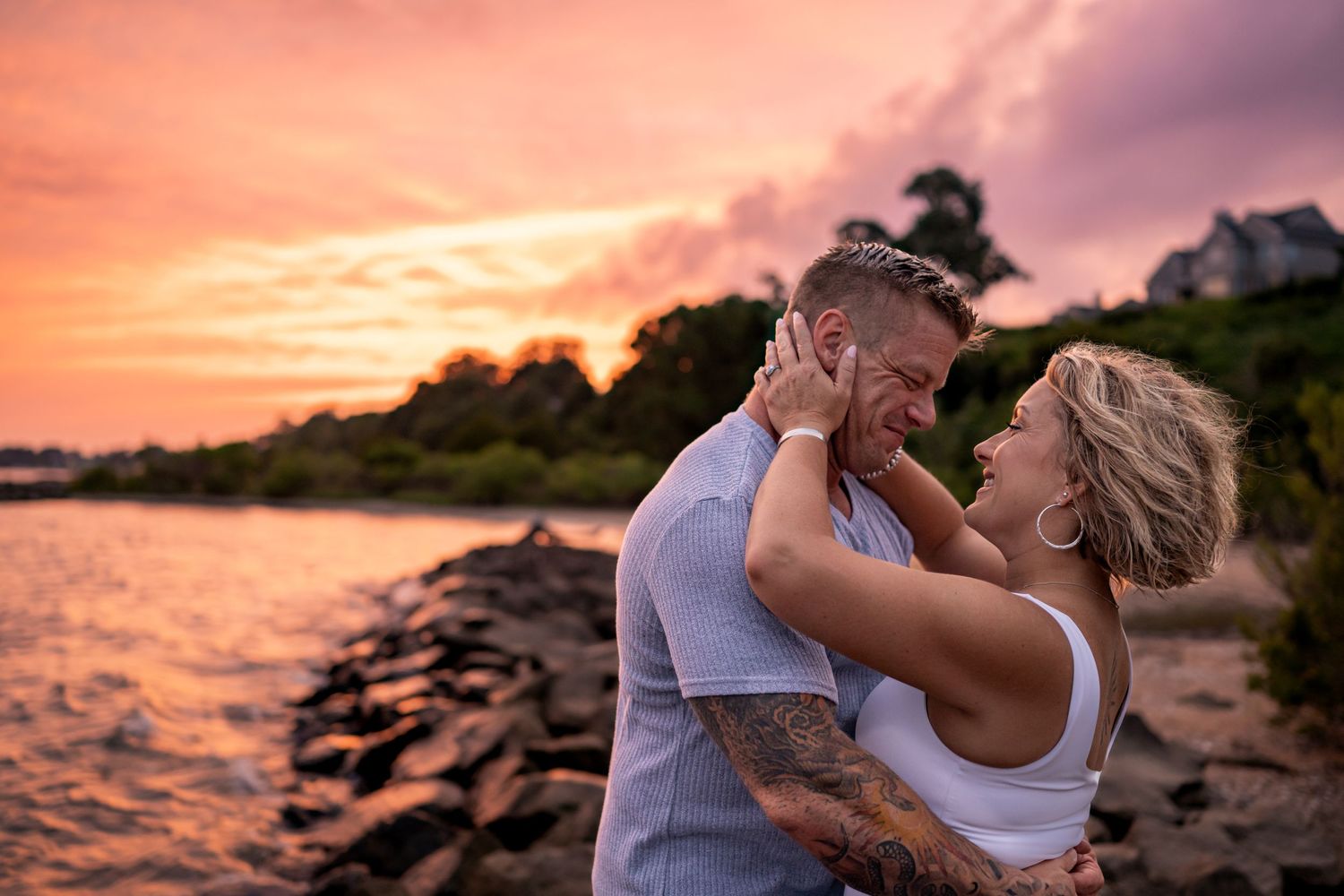 A romantic sunset embrace on a rocky beach with dramatic orange and purple sky.