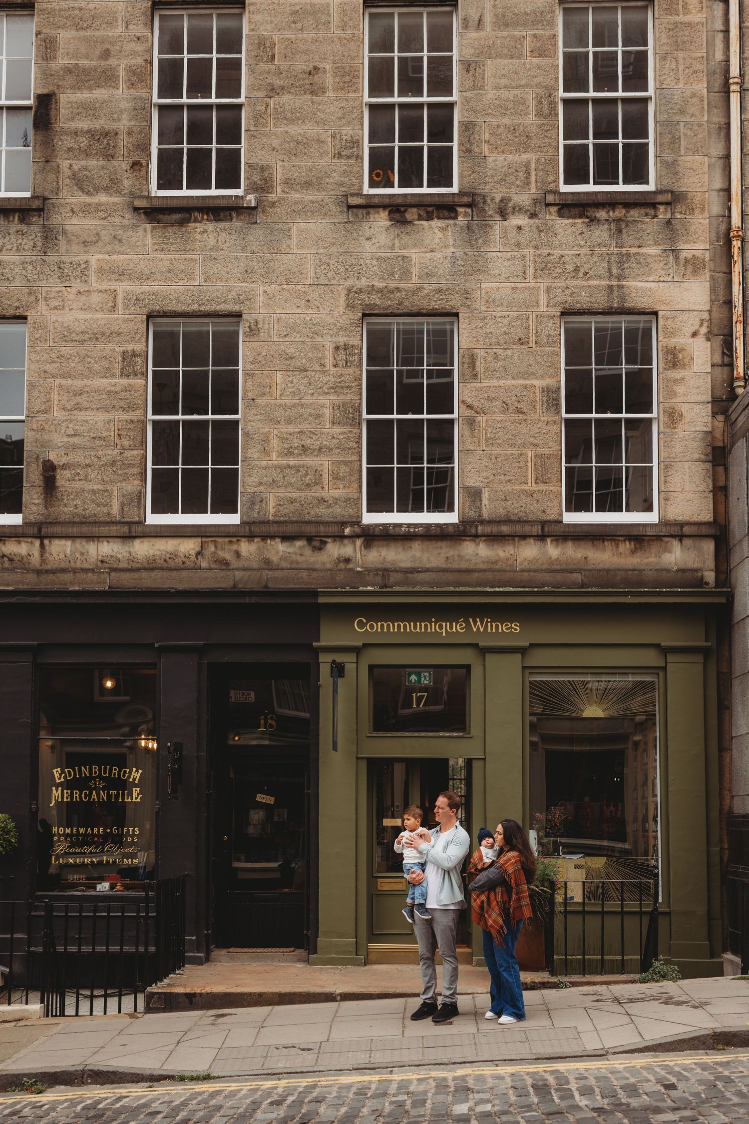 Historic stone building facade with green storefronts and traditional sash windows along a cobblestone street in Edinburgh.