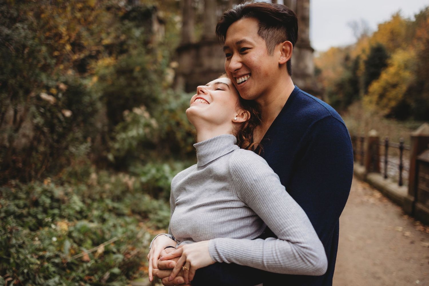 A romantic couple shares a joyful moment together on an autumn path surrounded by fall foliage.