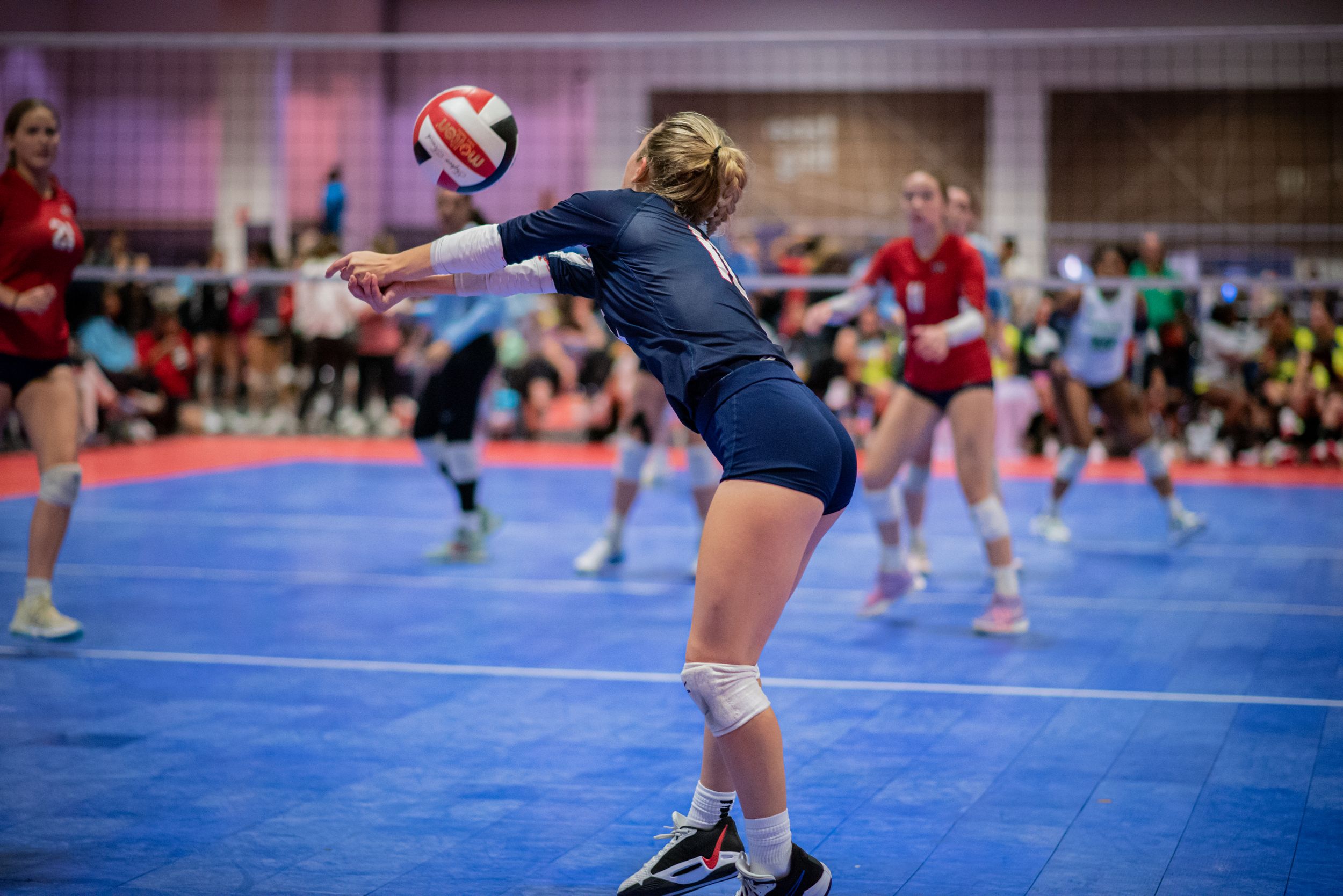 Female volleyball player in navy uniform executing a forearm pass during an indoor tournament match on blue courts.