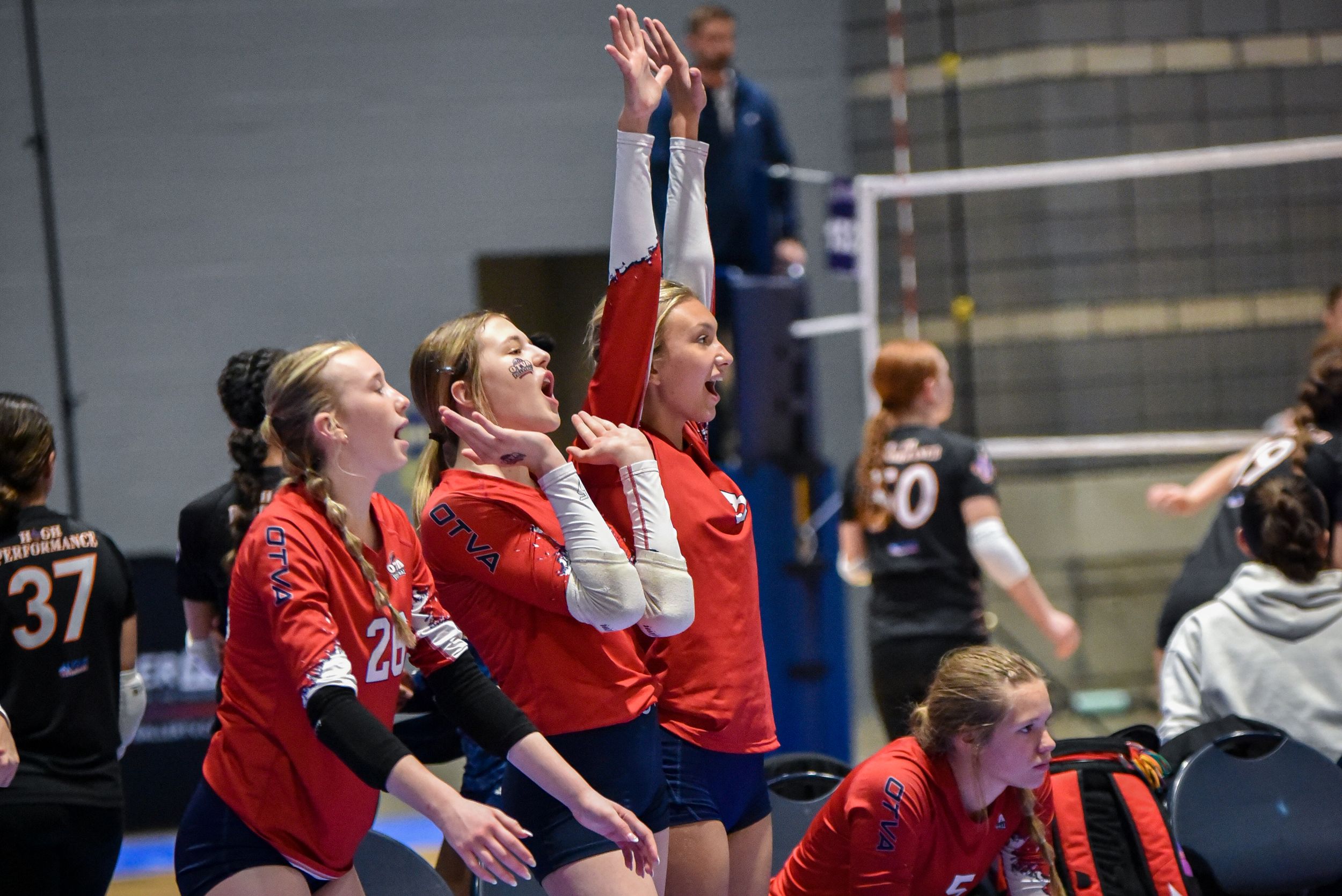 Female volleyball players in red uniforms celebrate enthusiastically during a competitive indoor volleyball match.