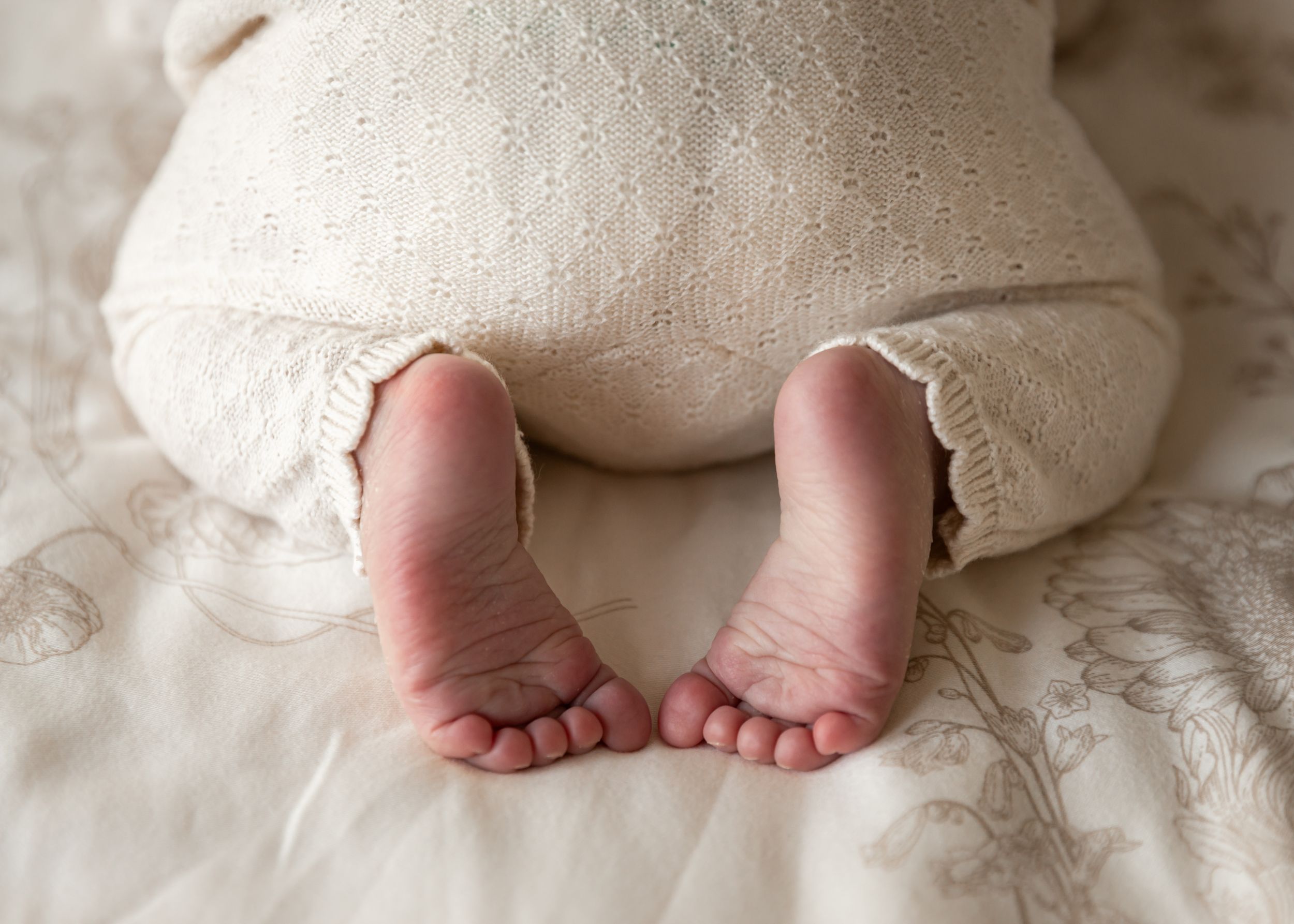 artistic photo of newborn feet in sleeping position for newborn photoshoot in soft beige colours