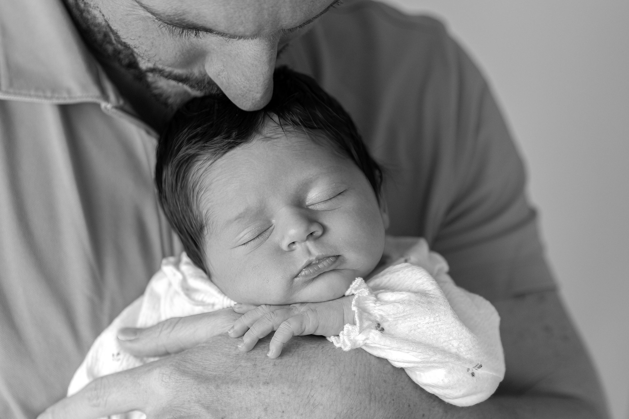 Carlene Thurston Photography - `at-home newborn photoshoot Dubai Close up photo of baby in dad's hands getting a kiss on the head