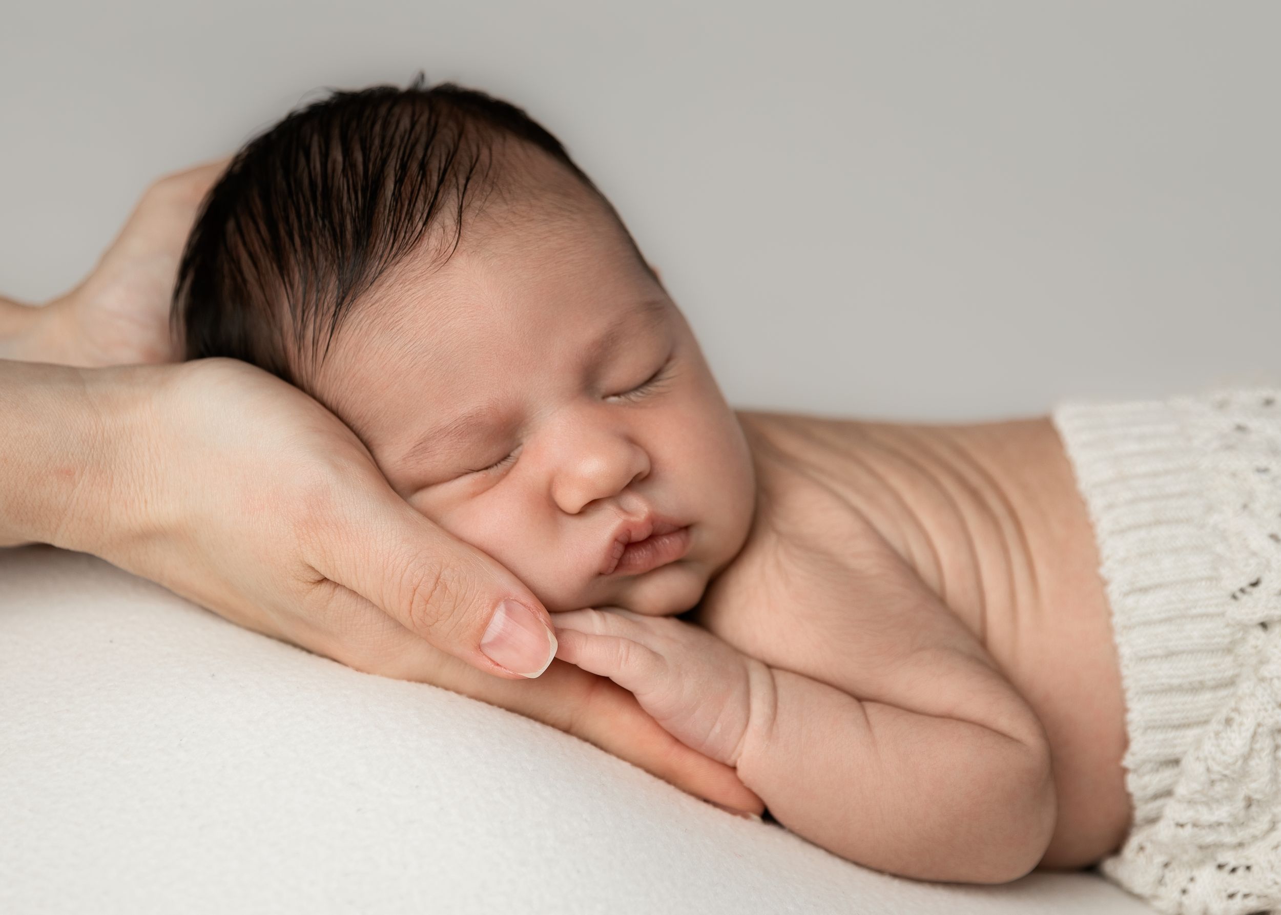 Baby sleeping on tummy head supported in mother's hands for newborn photoshoot