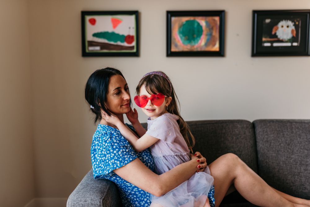 A heartwarming family moment on a grey couch with sunlight streaming through decorative framed art hanging on the wall.