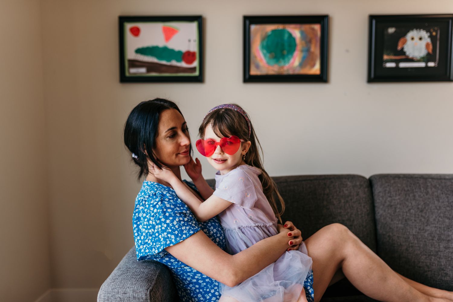 A heartwarming family moment on a grey couch with sunlight streaming through decorative framed art hanging on the wall.