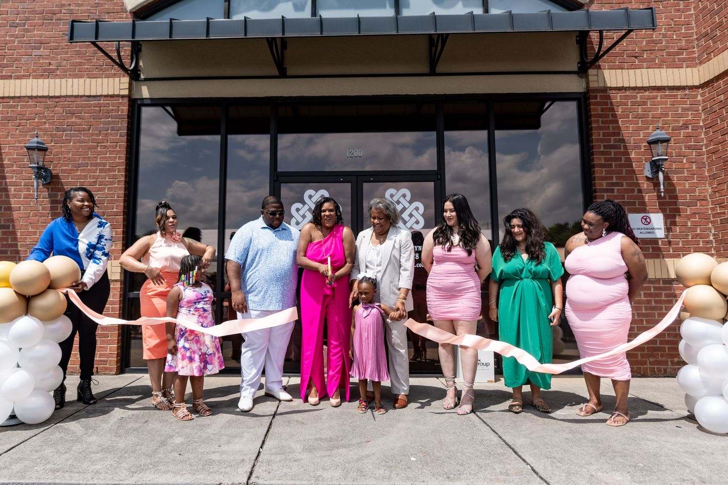 A group photo outside a building with people wearing colorful formal dresses in pink, green and other pastel shades.