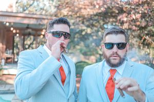 A group in matching powder blue suits and orange ties pose playfully together outdoors.