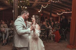 A couple shares their first dance in a rustic barn venue decorated with string lights and wooden beams.
