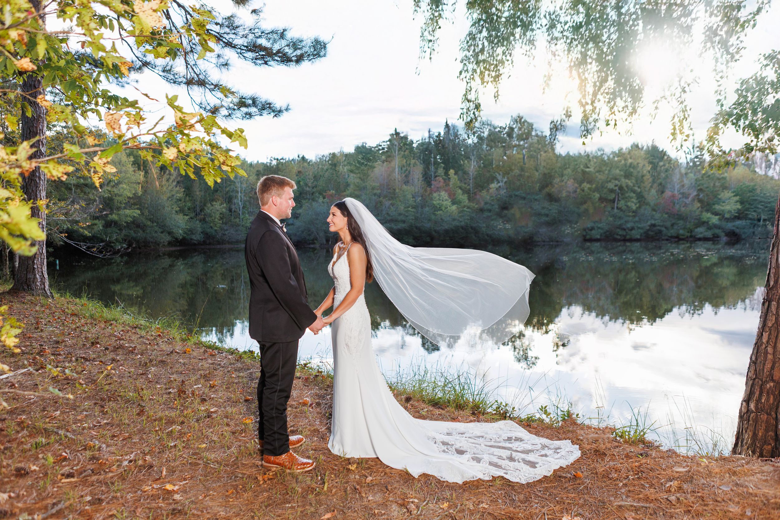 Romantic lakeside wedding photoshoot with couple posing against scenic autumn backdrop and willow trees at sunset.