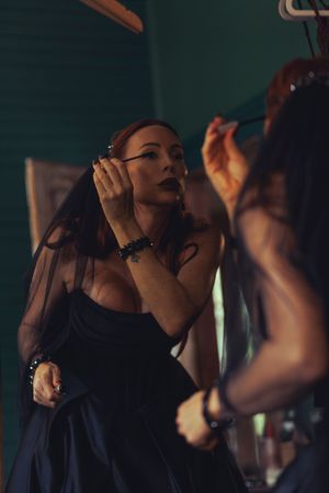Person applying makeup in front of a mirror in dark lighting conditions.