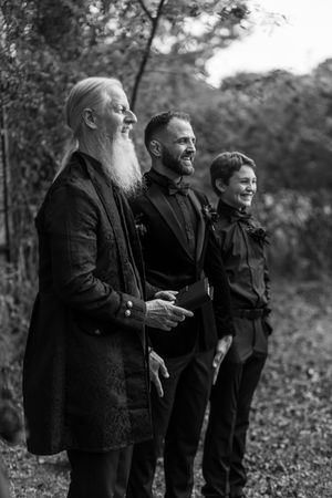 Three people in dark coats stand together outdoors in a black and white nature scene.