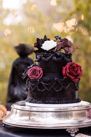 Elegant black gothic wedding cake decorated with red roses and intricate lace patterns on a silver cake stand.