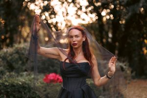 A figure in a black dress dances gracefully outdoors at sunset with bokeh lights in the background.