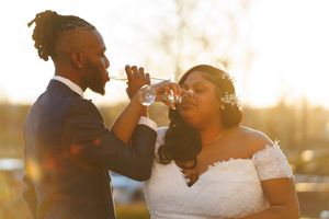 Elegant couple in wedding attire share a drink together during golden hour at sunset.