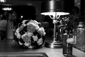 Black and white floral arrangement beside a table lamp and decorative glass bottle on a dark surface.