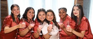 A group in matching red striped pajamas toasts with glasses while smiling at a festive gathering.
