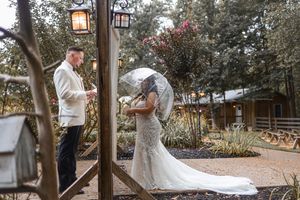 A romantic outdoor wedding ceremony takes place under rustic wooden posts in a garden setting.