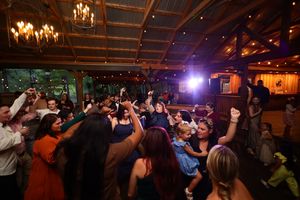 Energetic crowd dancing and enjoying music on a dimly lit dance floor with chandelier lighting above.