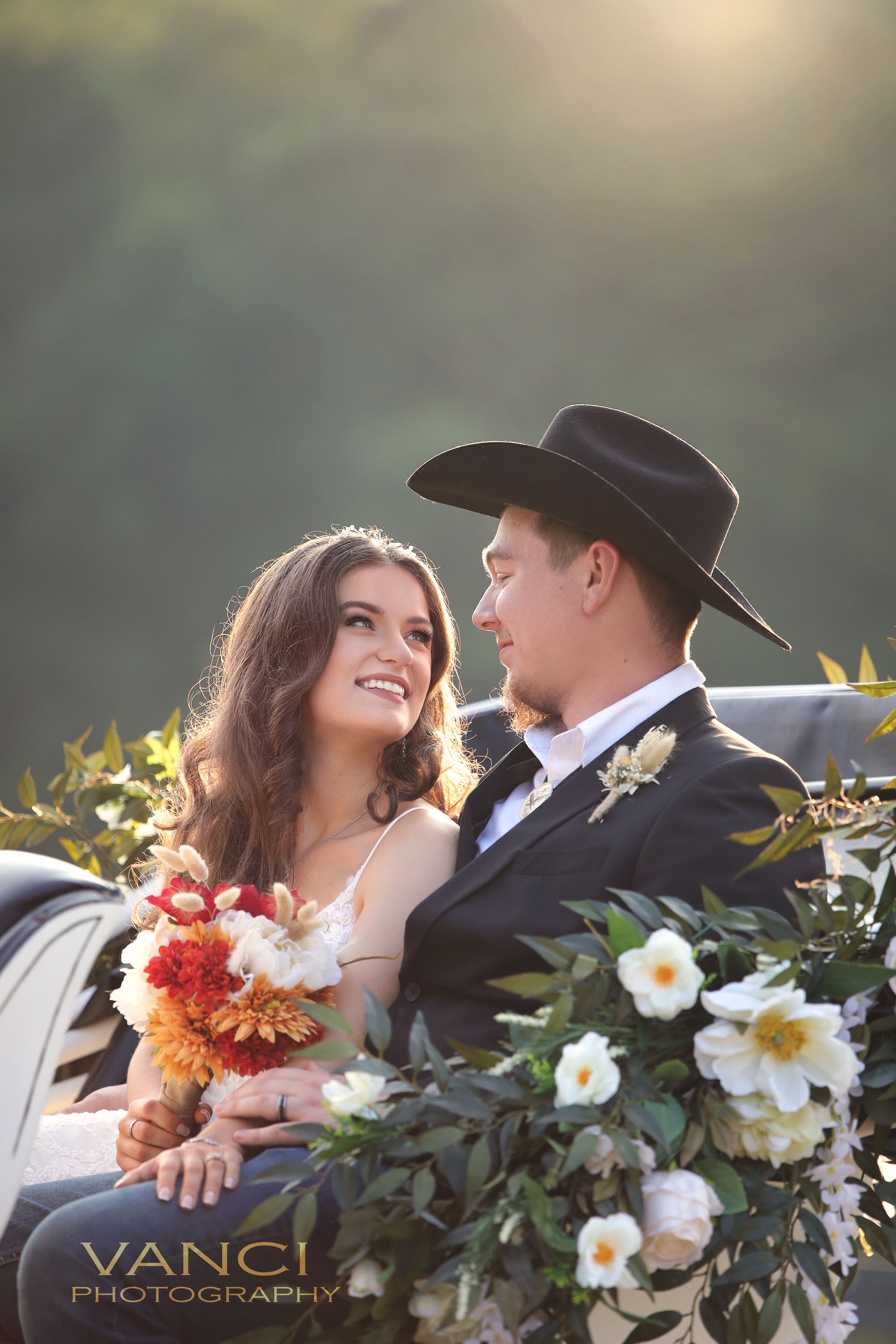 A western-themed wedding photo with flowers featuring a cowboy hat and romantic floral arrangements at sunset.