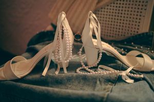 Elegant white bridal heels with pearls and decorative details displayed on a textured surface in vintage style lighting.