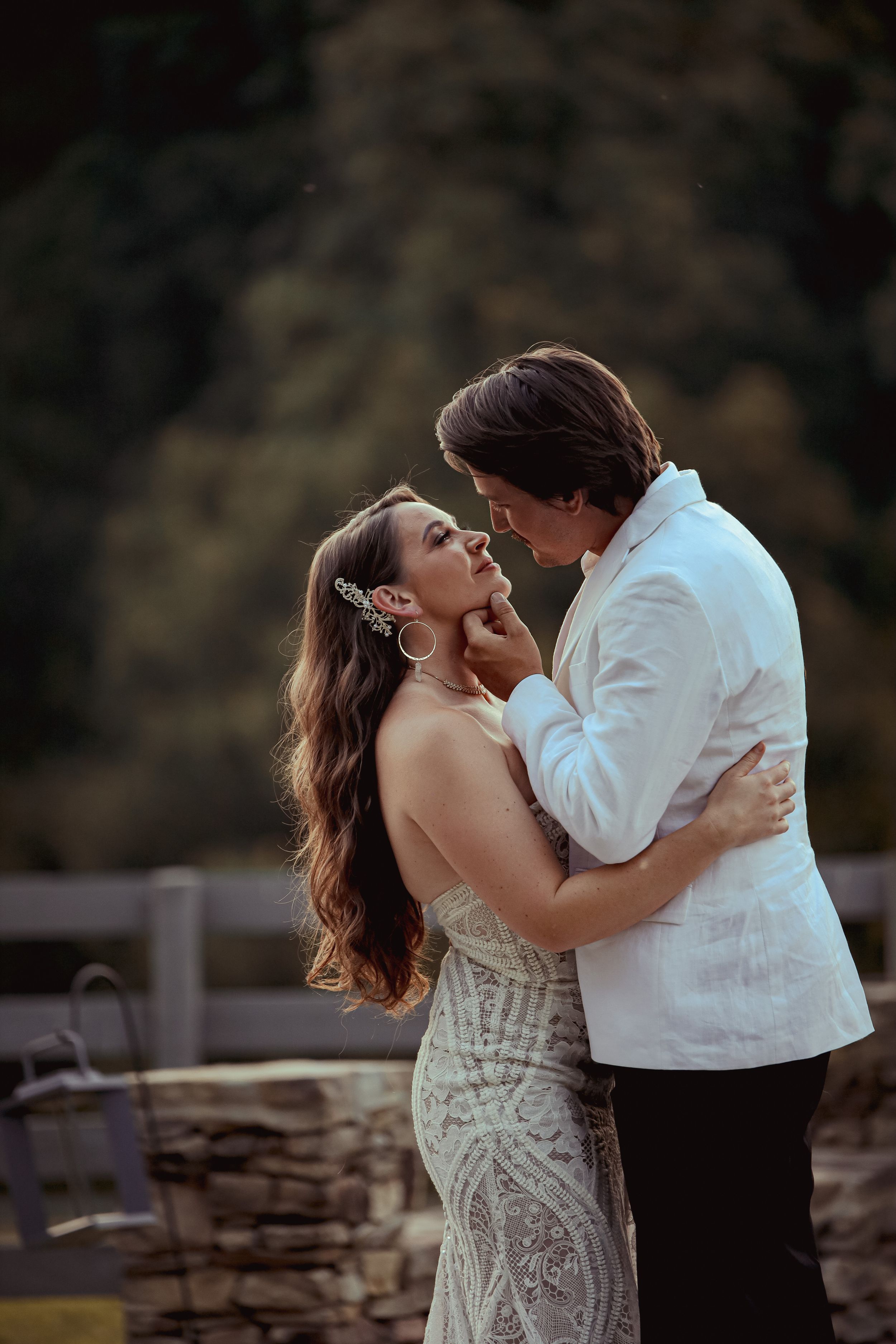 A romantic couple shares an intimate dance together outdoors against a natural backdrop at sunset.