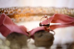 Wedding rings nestled on pink ribbon with soft bokeh lighting effect in background.