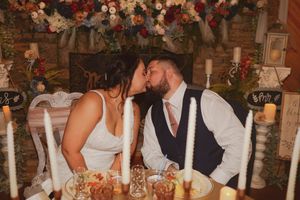 Newlyweds share a romantic kiss at their reception table decorated with floral arrangements and rustic decor.