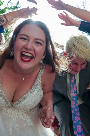 Joyful wedding celebration with guests raising hands in celebration under bright sunlight.