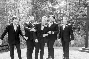 A group of groomsmen in formal attire sharing a candid moment in a black and white photo.