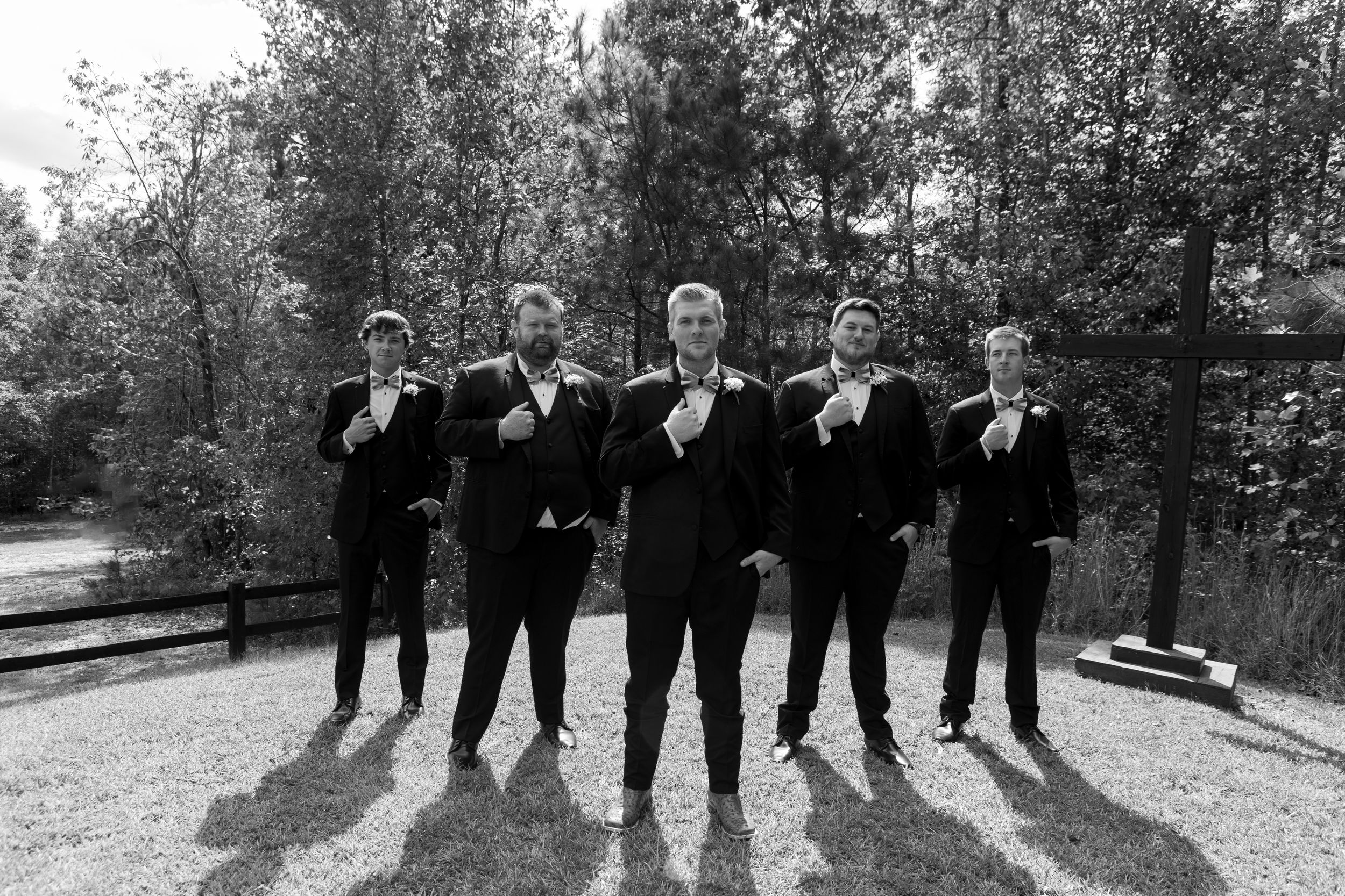 Groomsmen in black suits pose together outdoors creating silhouettes against a natural backdrop.