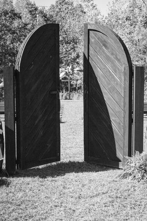 A black and white photograph of large wooden gates opening to reveal a garden space beyond.