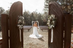 Wedding ceremony setup with wooden archway and white floral decorations in an outdoor garden setting.