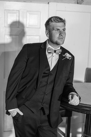 Classic black and white photos of person in formal suit posing against white interior backdrop.
