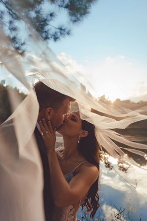 Romantic sunset wedding photo with flowing veil creating ethereal effect against dramatic sky.