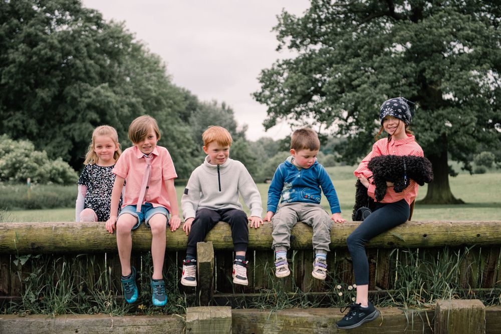 Seven pairs of legs dangling over a stone wall showcase colorful socks and casual footwear in an outdoor setting.