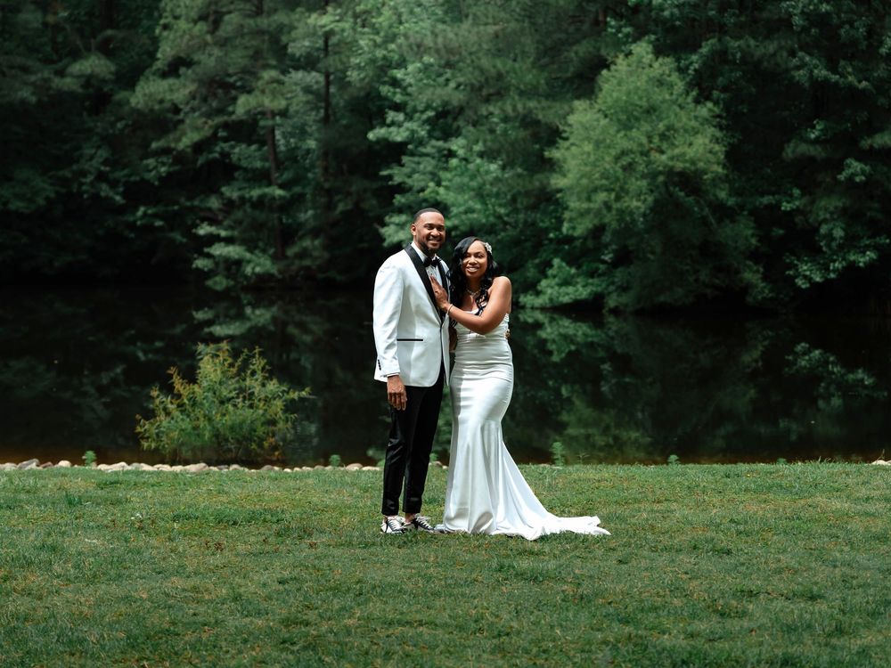 A couple in wedding attire shares intimate moments in a lush green outdoor setting during their wedding celebration.