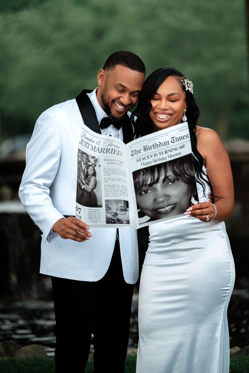A couple in formal attire shares intimate moments while reading a newspaper together in a romantic outdoor photoshoot.