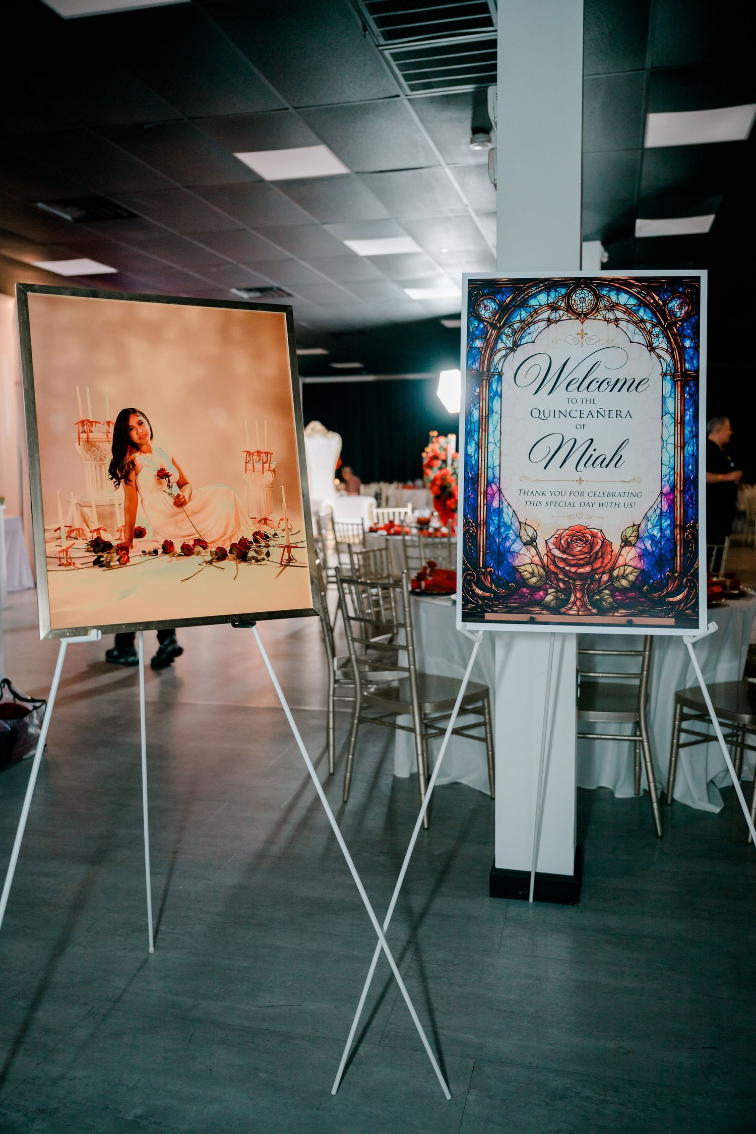 Welcome sign for Miah's Quinceañera with a stained glass rose design beside a portrait on an easel in a banquet hall.
