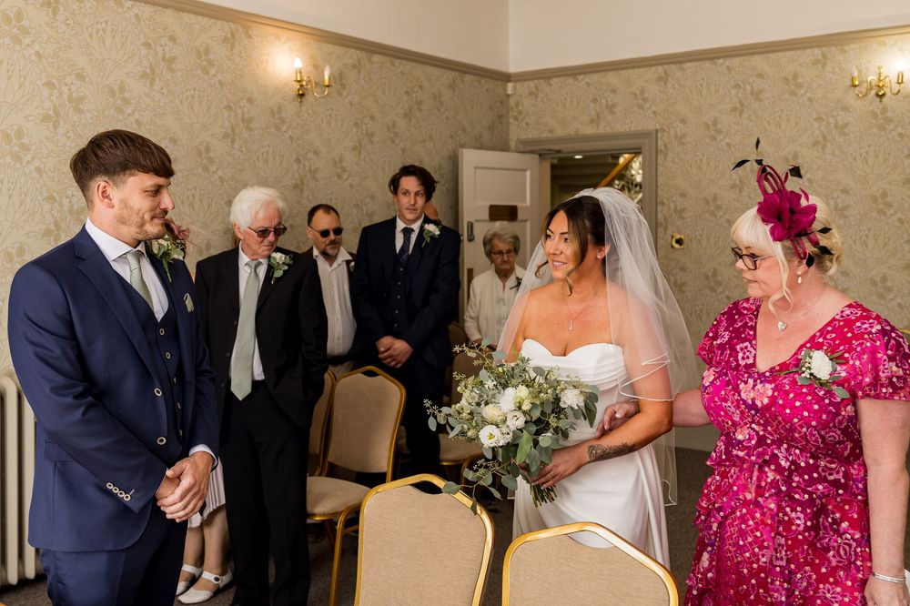 Bride in white gown and veil meets groom in navy suit at wedding ceremony entrance.