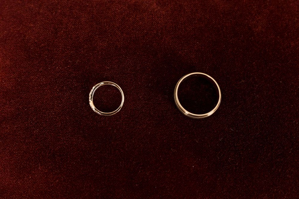 Two gold wedding bands resting on a dark red velvet surface, one smaller and one larger.