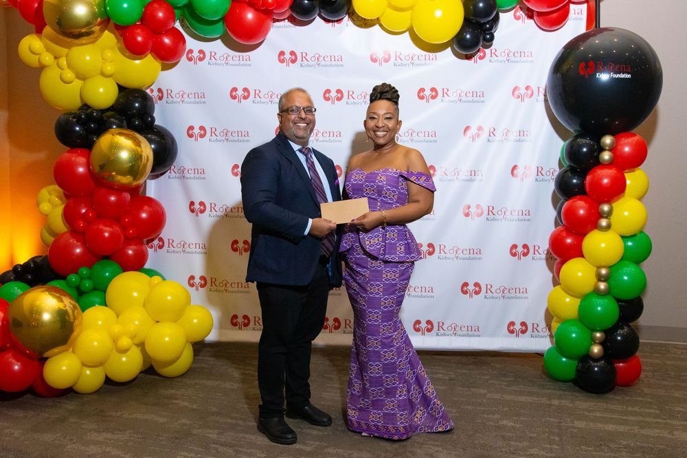 Two people pose together at a formal event with colorful balloons in red, black, gold, and green at a gala.
