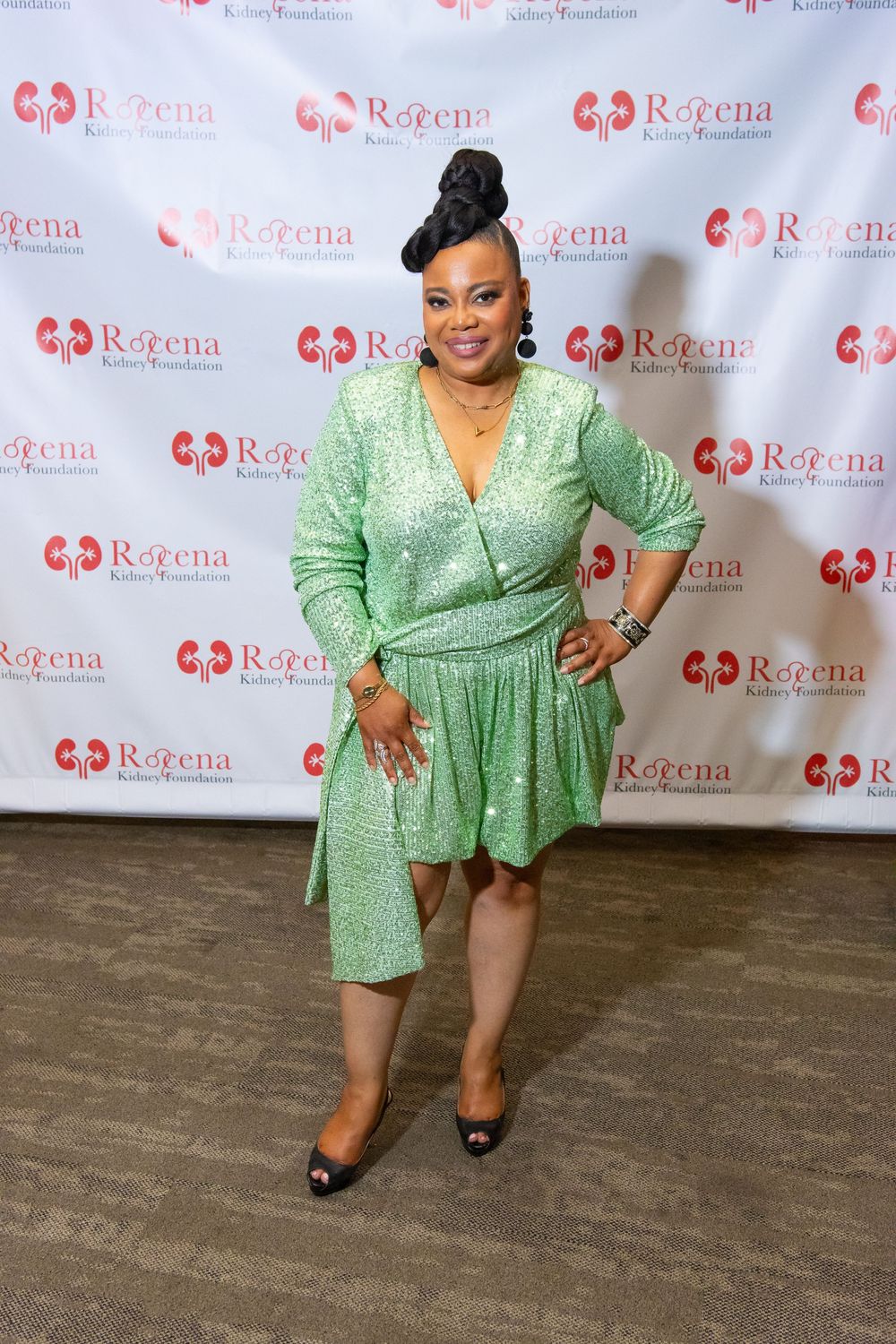 Woman in green sequin dress posing at Rozena Kidney Foundation event backdrop.