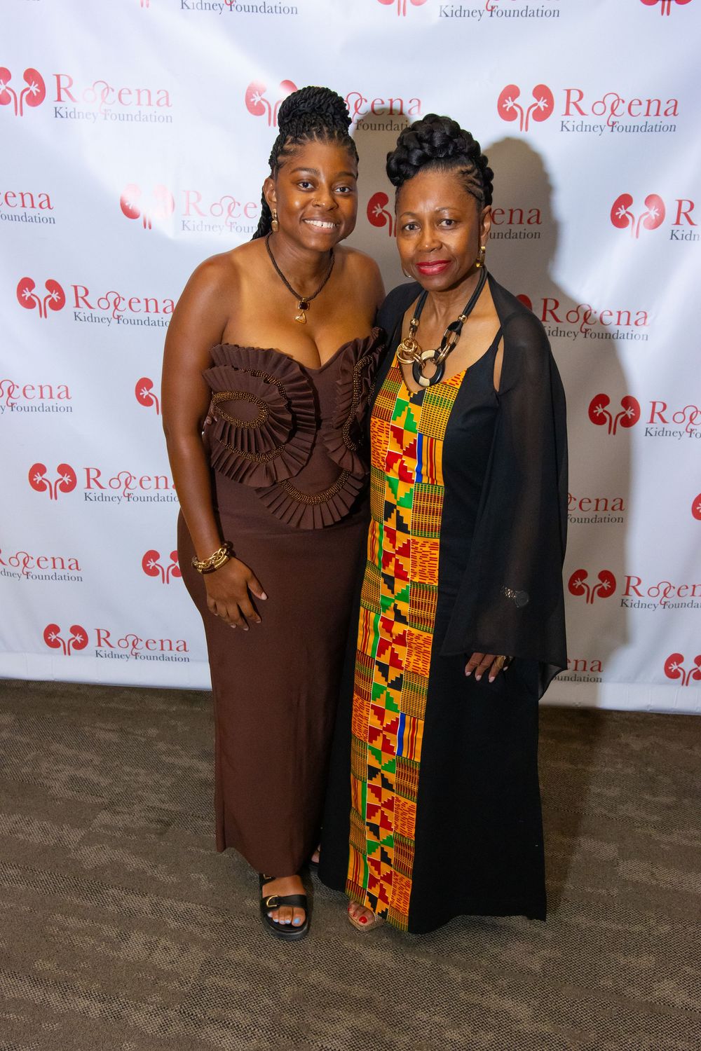 Two women posing together at Rogena Kidney Foundation event, wearing elegant brown and colorful kente cloth outfits.