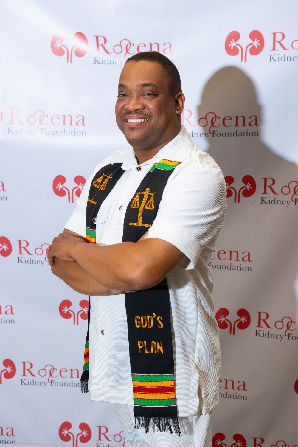 Man in white shirt with Kente cloth stole reading Gods Plan poses at Rotena Kidney Foundation event.